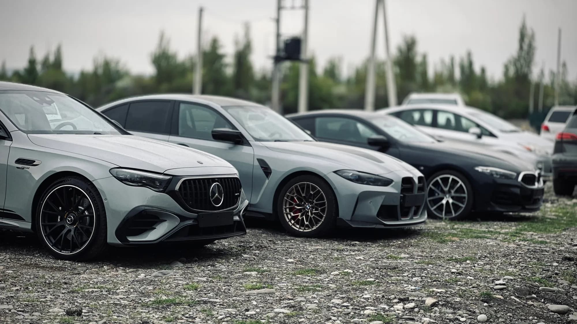 Mercedes-AMG and BMW M cars lined up on gravel, waiting to load